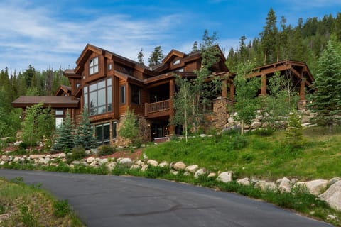 Mountain lodge architecture nestled among towering evergreens with natural stone landscaping and private driveway access.