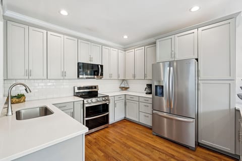 Your fully equipped kitchen features gleaming stainless steel appliances, pristine white cabinetry, and warm hardwood floors—perfect for preparing meals during your stay.