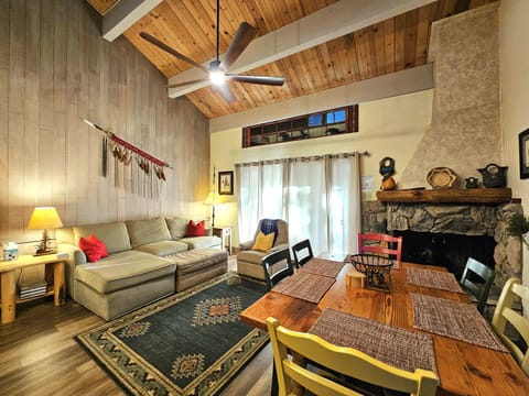Open living area with sofa, recliner, six-seat dining table, fireplace, ceiling fan, sliding doors, lamps, and wall art.