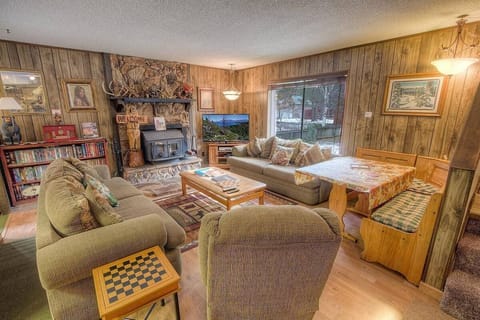 Living room with fireplace, flat-screen TV, sofa seating, armchair, large window, bookshelf, and dining nook.