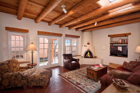 Spacious living area has kiva fireplace, grand Vigas, and Santa Fe blue sky