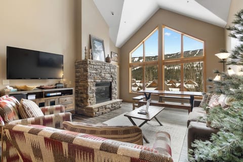 Unwind in your cozy living room with soaring ceilings, stone fireplace, and stunning mountain views through expansive windows.