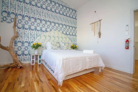 Sunlit, boho-inspired bedroom with warm wood floors, cozy linens, and charming artistic details for a calm, inviting stay.
