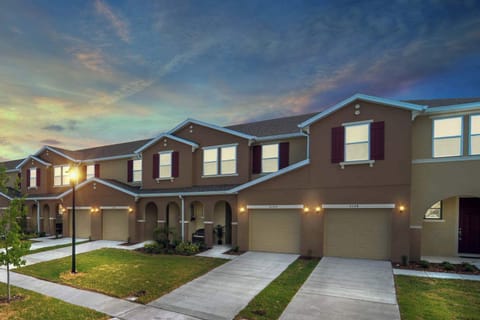 Sunset-lit modern townhouse row with warm stucco, burgundy shutters, attached garages and welcoming arched porches - an inviting, family-friendly spot to call home during your Compass Bay getaway.