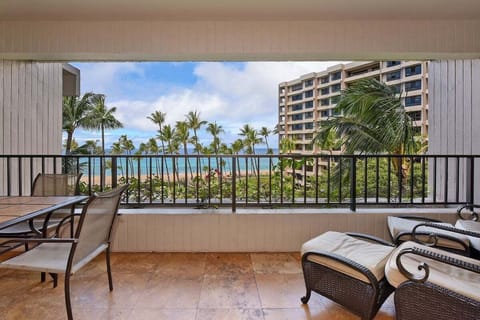 Spacious ocean-view balcony with cushioned loungers and a four-seat dining set, perfect for relaxing or enjoying meals while overlooking swaying palms and turquoise waters.
