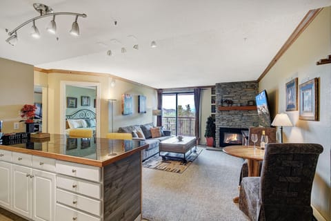 Open living area with stone gas fireplace, wall-mounted TV, and sliding glass door to balcony with mountain views.