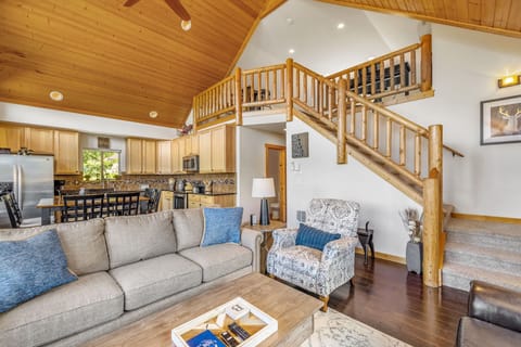 Open-concept living with exposed wood beams, cozy furnishings, and a rustic-style staircase centerpiece