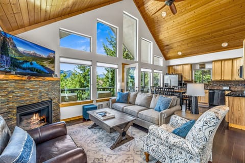 Vaulted living room with soaring windows, stone fireplace, and panoramic mountain light