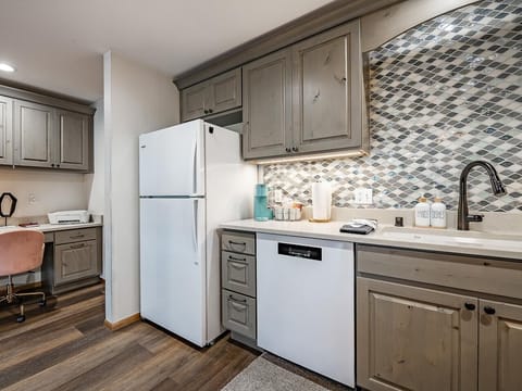 Kitchen features distressed wood cabinets, a white fridge, dishwasher, and a mosaic tile backsplash.
