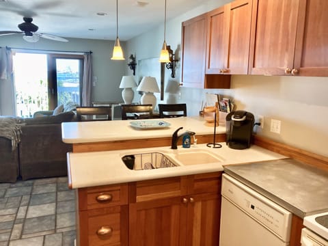 Kitchen sink, dishwasher, bar, and view of living room and balcony.