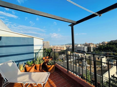 Enjoy breathtaking views of the Barcelona skyline from the comfort of this private terrace, complete with a lounge chair and potted plants. The terrace features a pergola for shade and a black metal railing.