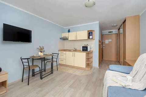 A view of the open kitchen with light wood cabinets and essential appliances. It’s compact yet functional for all cooking needs.