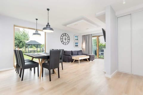 A bright dining area featuring a dark wood table with six black chairs, illuminated by modern pendant lighting, and complemented by large windows bringing in natural light.
