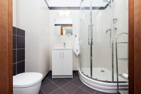 A modern bathroom featuring a glass-enclosed shower, a toilet, and a sink. The design is clean and minimalist with contrasting dark and white tiles.