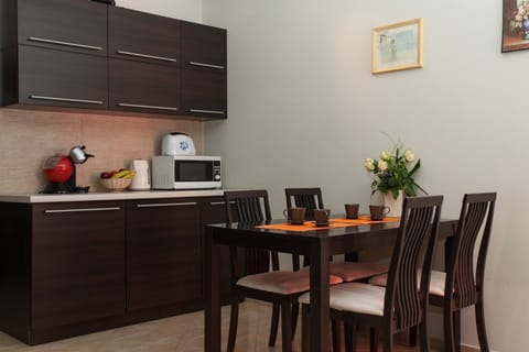 A compact kitchen area with dark wood cabinets, featuring basic appliances such as a microwave and a coffee maker. A small dining table with chairs is neatly arranged beside it.