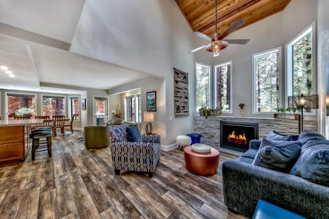 Relax in your spacious living room featuring soaring ceilings, cozy fireplace, and stunning forest views through oversized windows.