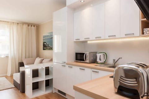  A sleek, modern kitchenette with white cabinets, integrated appliances, and light wood floors. A small dining table with chairs is nearby.