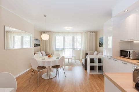 An open-plan living room with a kitchenette. The sofa is light-colored, and the room has a modern, minimalistic design with wooden floors and sleek furniture.