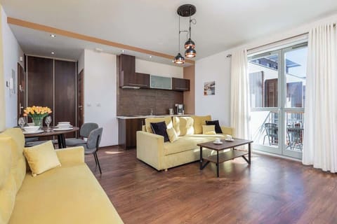 A spacious living room with a cream-colored sofa, dark wooden floors, and a large window providing ample natural light.