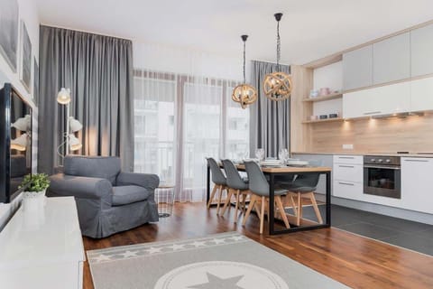 Bright, spacious living room with kitchenette. The grey long curtains bring a lot of cosiness and the soft grey armchair provides a relaxing and restful environment. Dining table for 6 people.