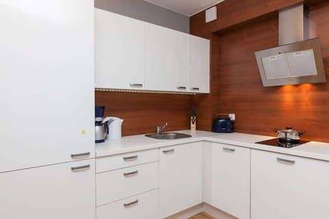 A modern kitchenette with white cabinet fronts, fully equipped with appliances. The dining area includes a minimalist table with chairs. The space is light and airy, with soft wood accents adding warmth.