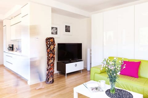 Another angle of the living room showing a white console and green sofa with pink and purple pillows. A modern, minimalist aesthetic is enhanced by colorful decor and soft lighting.
