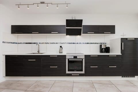 A sleek kitchen with dark cabinetry, a tiled backsplash, and modern appliances.