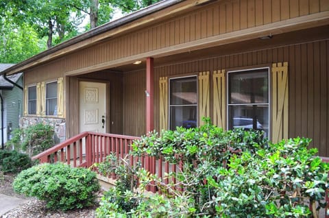 Charming wood-sided cottage nestled among lush greenery with a welcoming covered porch and decorative shutters. Surrounded by mature trees and landscaped gardens, the property offers a peaceful retreat.