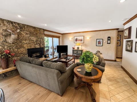 Living room with gray upholstered sofas, stone fireplace, hardwood floors, and sliding glass door to balcony.