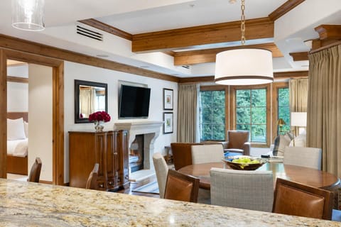 Granite countertop foreground leads to dining area with mixed wood and fabric chairs under a drum pendant.