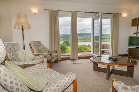 Full height windows with door to patio, seating and views of Loch Awe and garden