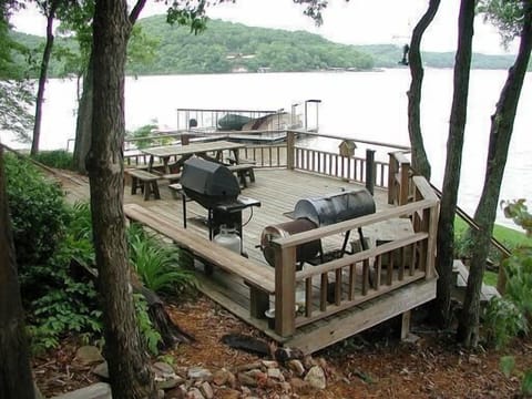 Deck is shaded by umbrella of trees with tiki lights I outdoor dining furniture