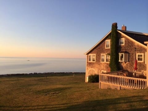 View of house and deck with expansive lawn area with seawall and beach.