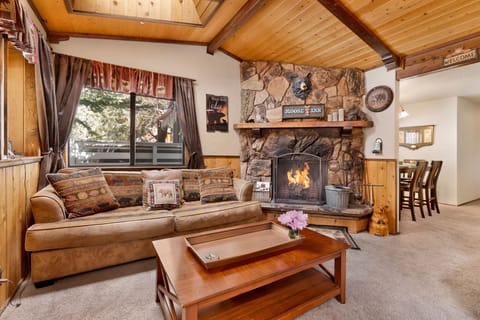 Cozy mountain living room with wood ceilings, stone fireplace, comfy seating, and smart TV—perfect for relaxing evenings, movie nights, and warm cabin vibes after outdoor adventures.