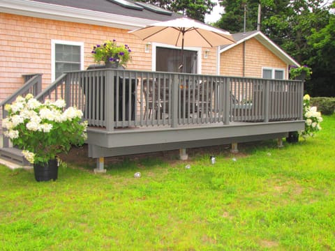 Back yard with large deck ,couch,  dining table and gas grill and grassy yard.