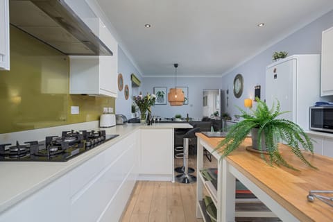 White gloss handle-less kitchen with stone worksurfaces - dining area beyond