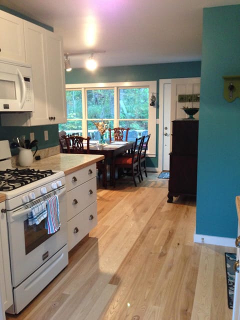 Kitchen opens to dining and living room areas, with views of back deck and woods.