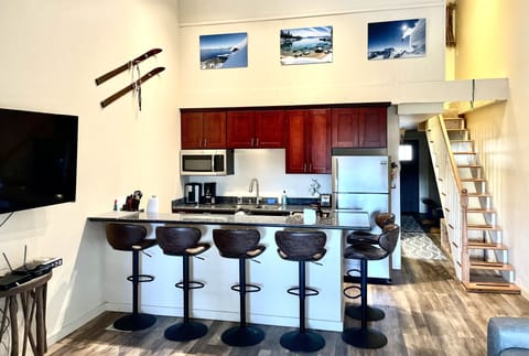 Kitchen, barstools, large TV and stairs that lead to two small bedrooms upstairs