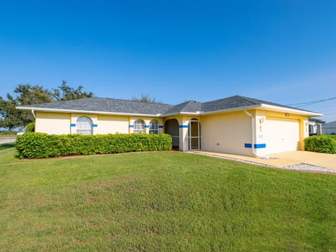 Single-story villa with pale yellow stucco walls, blue trim, and a two-car garage under a gray shingle roof.