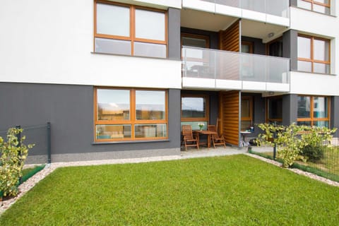 The exterior of a modern apartment building with a well-maintained green lawn and balconies overlooking the outdoor space.