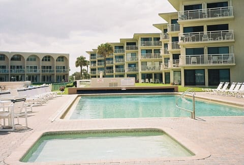 View of condo from deck of childrens & adult pool encircled by lounge chairs.  