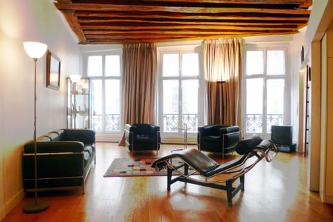 Living area offers 3 tall windows, wooden floor and wooden beams