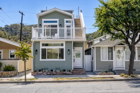 Charming two-story coastal home featuring a spacious balcony overlooking rolling hills, nestled in a quiet residential neighborhood with tree-lined streets and mountain views.