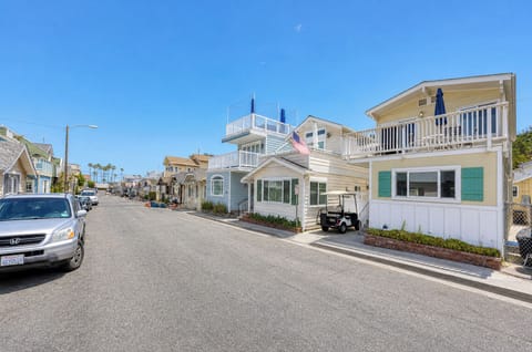 A charming coastal neighborhood featuring colorful beach cottages with upper balconies, palm trees dotting the horizon, and convenient street parking along a peaceful residential road.