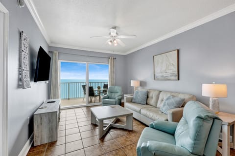 Living area features sliding glass doors leading to balcony, leather sleeper sofa, 2 leather recliners and a wall mounted Smart TV 