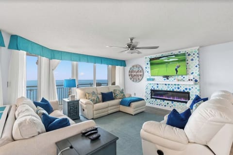 The living room is equipped with ample seating space, an electric fireplace, and a massive 65"+ t