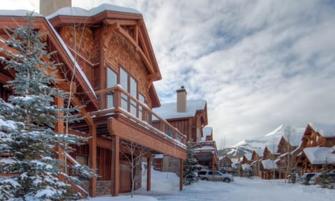Charming mountain lodge nestled in a snowy alpine village, with traditional timber architecture and stunning mountain peaks creating the perfect winter retreat backdrop.