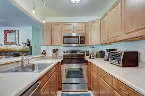 A modern kitchen with stainless steel appliances, light wood cabinets, a double sink, and small appliances like a toaster oven and coffee maker on the countertops.