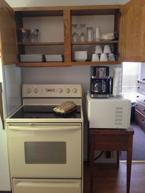 Kitchenette with electric range, coffee maker, toaster, microwave and dishware.