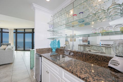 Wet bar area featuring granite countertops, ice-maker, blender, and elegant glassware display